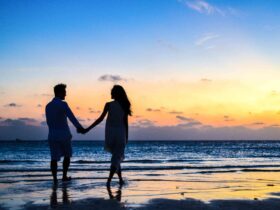 Man and Woman Holding Hands Walking on Seashore during Sunrise