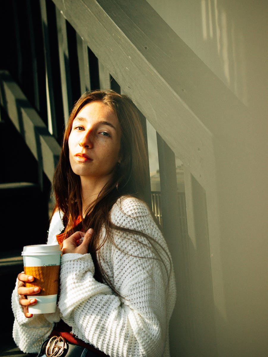 Young woman wearing white sweater drinking coffee