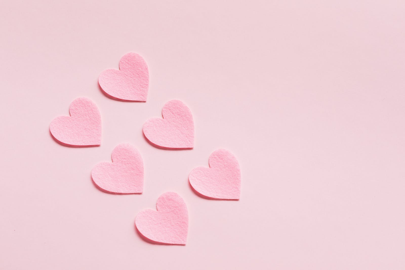From above of composition made with heart shaped papers cutout of rough uneven pink cardboard placed diagonally on light pink background