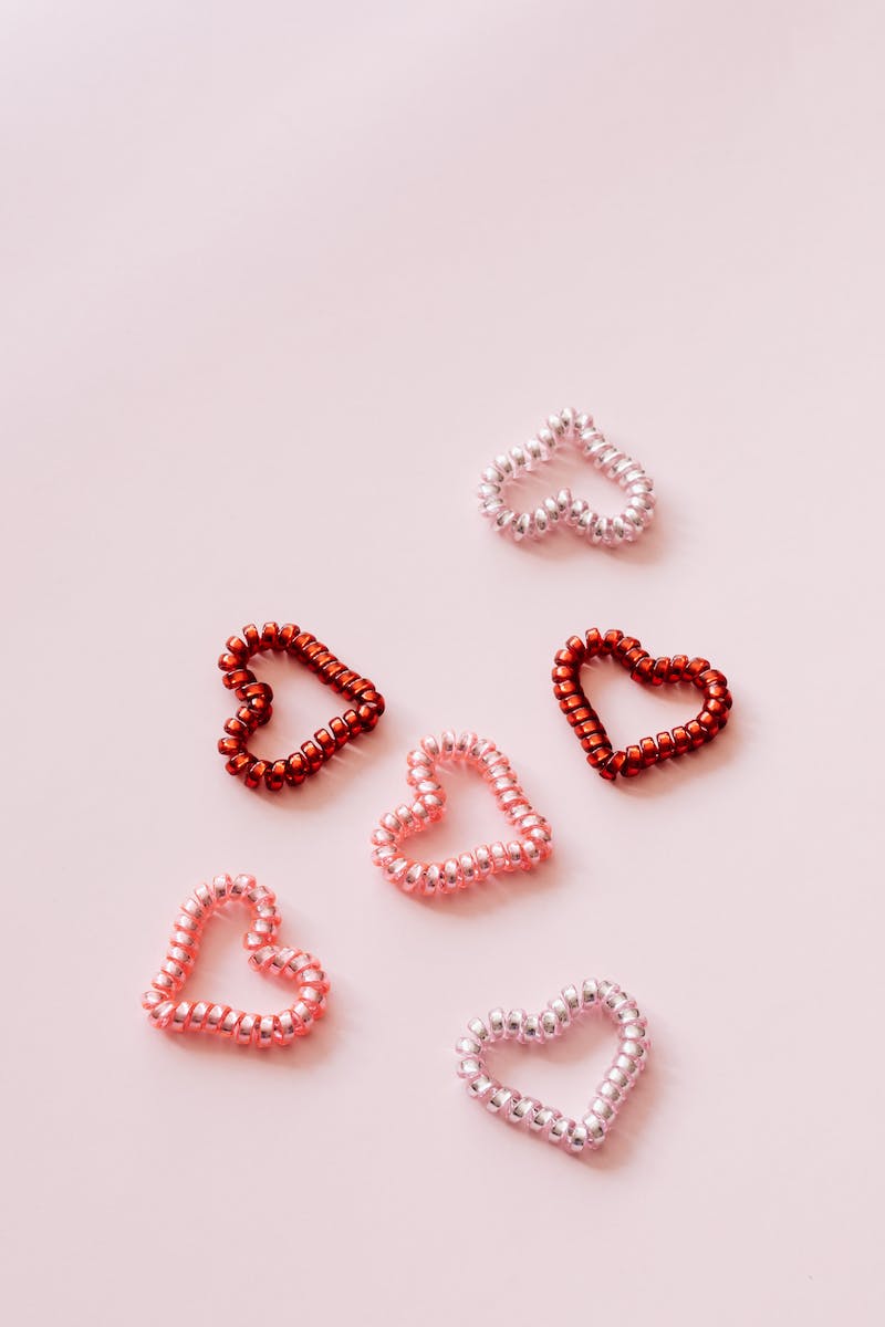 Top view of multicolored coil hair ties in shape of hearts composed on pink surface for Saint Valentines Day