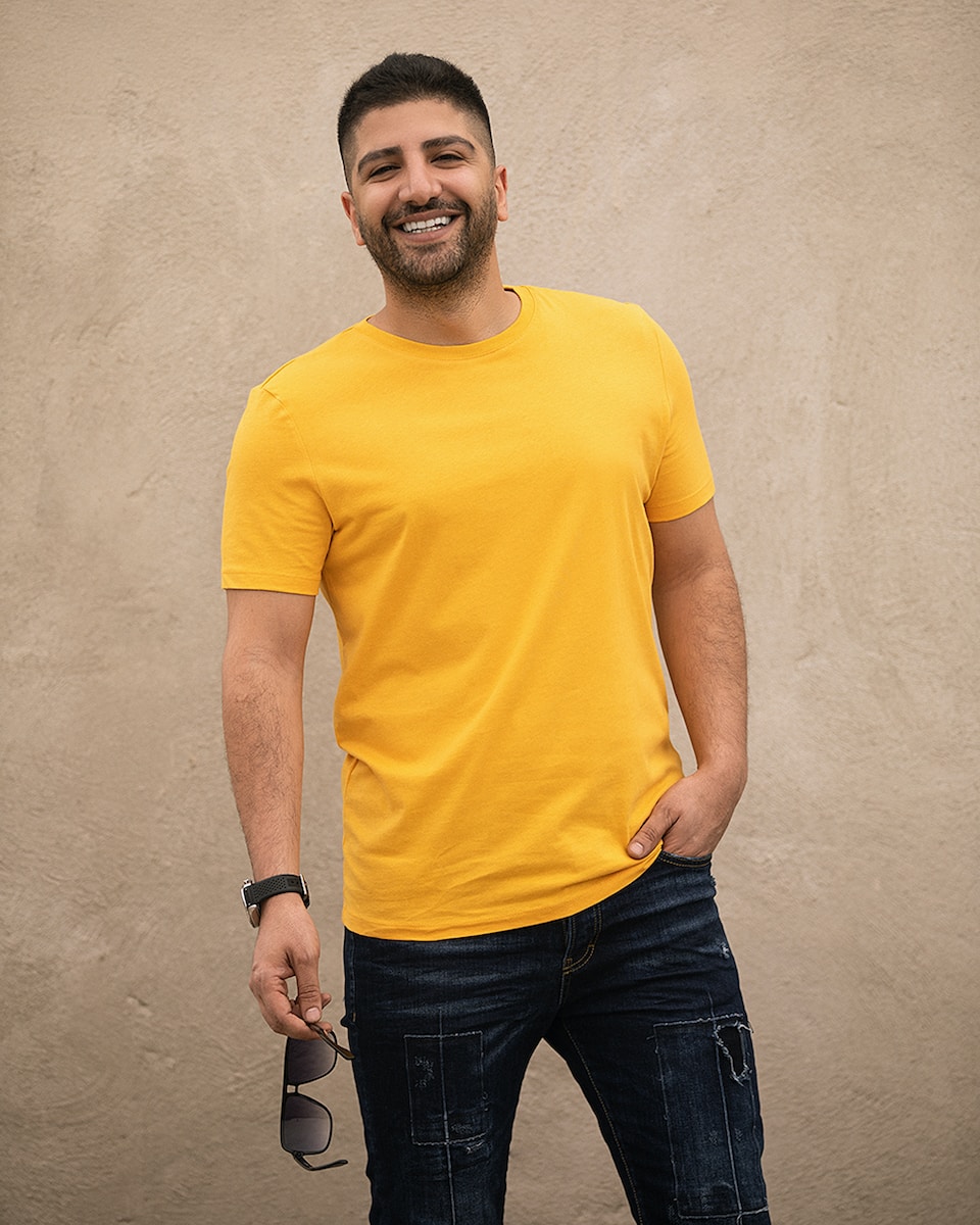 man in yellow crew neck t-shirt and black denim jeans standing beside white wall