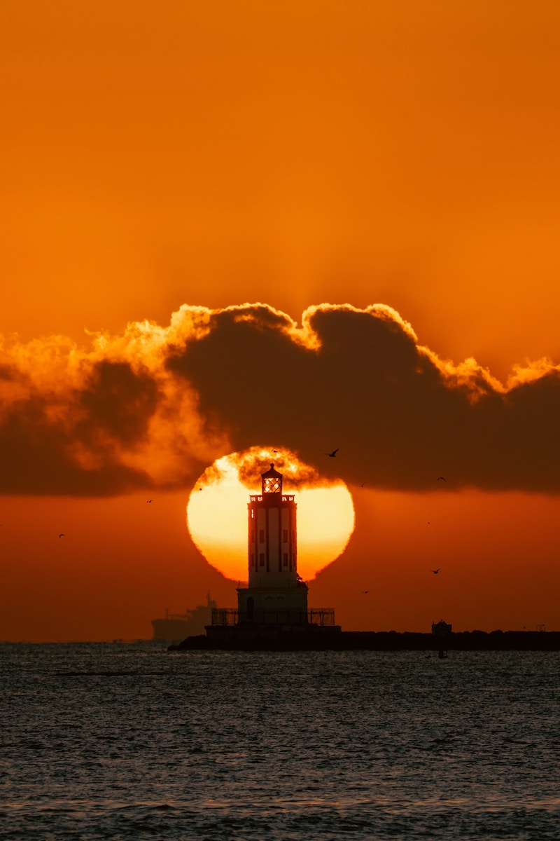 the sun is setting behind a lighthouse in the ocean