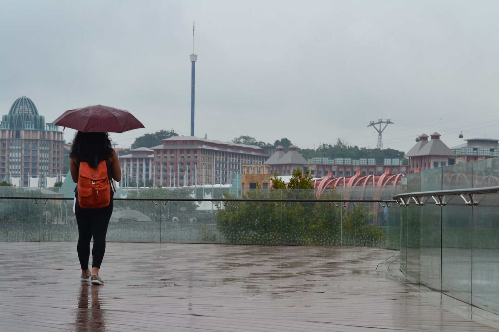 a woman with an orange backpack is walking in the rain with an umbrella