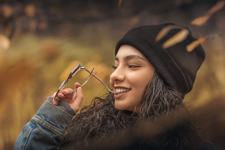 woman holding sunglasses wearing black knit cap