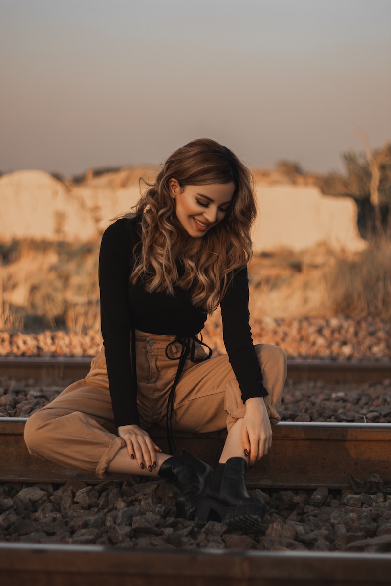 woman in black long sleeve shirt and brown pants sitting on brown wooden bench during daytime