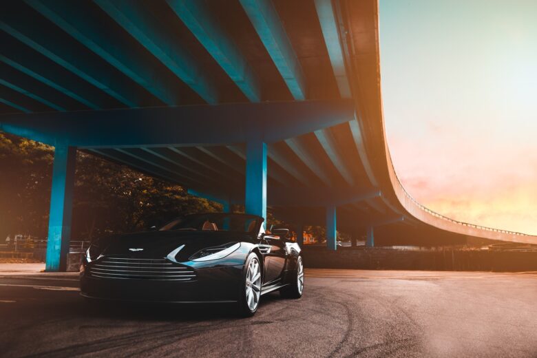 black Aston Martin convertible coupe parked beside blue concrete bridge