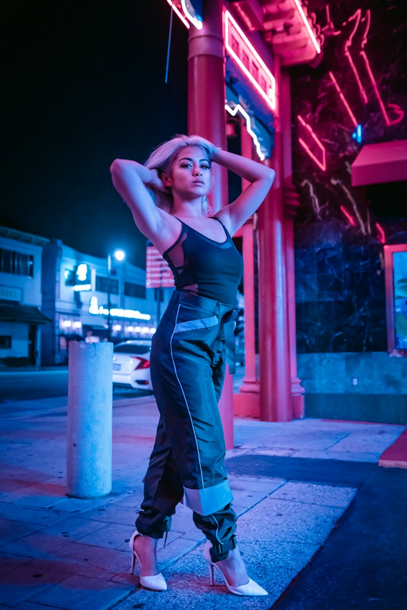 woman in black sports bra and blue denim jeans standing beside red neon light signage