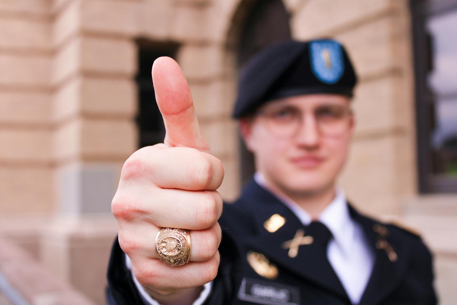 Close-up of military officer wearing uniform giving thumbs up gesture, ring visible.